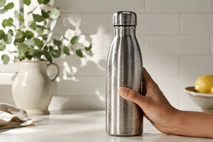 A runner's hand on a steel water bottle in morning kitchen light